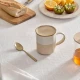 Δίχρωμη κούπα Kate της Secret de Gourmet σε λευκό και μπεζ χρώμα πάνω σε στρωμένο τραπέζι πρωινού.