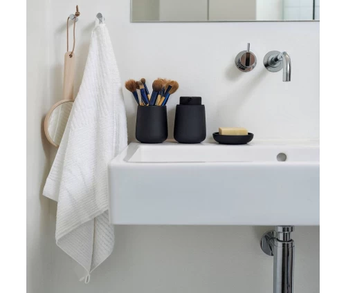 Σαπουνοθήκη Zone Denmark Nova One σε μαύρο χρώμα από stoneware με soft-touch, μαζί με θήκη για οδομτόβουρτσες και ντισπένσερ σε λευκό νιπτήρα.