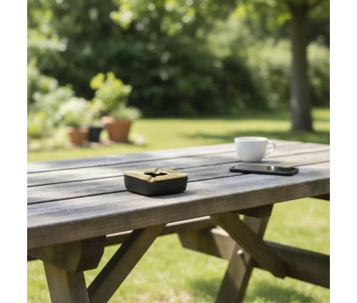 Σταχτοδοχείο Espiel ASR107 από αλουμίνιο, χρυσό καπάκι με μαύρη βάση, αντιανεμικό τετράγωνο 10,5εκ, επάνω σε τραπέζι σε εξωτερικό χώρο.