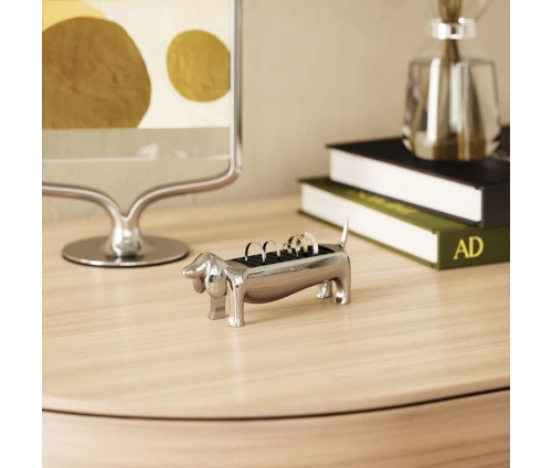 Μεταλλική βάση κοσμημάτων Umbra Dachsie σε σχήμα σκύλου λουκάνικο (dachshund), σε φυσικό χώρο δίπλα από βιβλία.