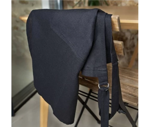 Κοντινό πλάνο σε μαύρη ποδιά Finesse CHEF ριγμένη σε ξύλινη καρέκλα, αναδεικνύοντας την ποιοτική βαμβακερή υφή και τον μεταλλικό κρίκο στο λουρί.