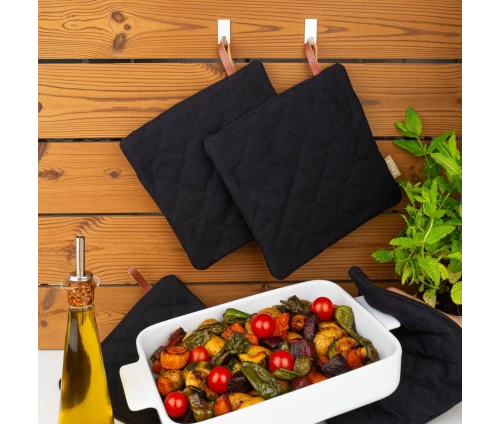 Μαύρες πιάστρες Finesse CHEF κρεμασμένες σε γάντζους και σε χρήση δίπλα από ένα ζεστό κεραμικό σκεύος με ψητά λαχανικά.