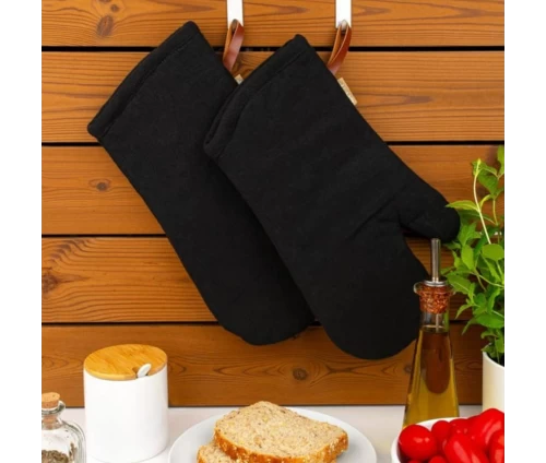 Μαύρα γάντια κουζίνας Finesse CHEF κρεμασμένα πρακτικά σε ξύλινο τοίχο, πάνω από τον πάγκο προετοιμασίας.