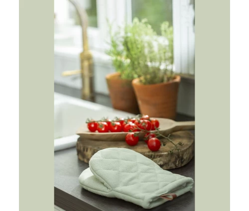 Παστέλ πράσινο γάντι κουζίνας Finesse CHEF ακουμπισμένο στον πάγκο της κουζίνας, δίπλα σε ένα ξύλο κοπής με φρέσκα ντοματίνια.