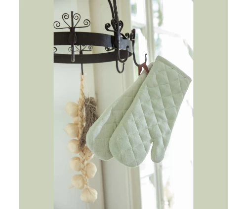 Παστέλ πράσινα γάντια φούρνου Finesse CHEF κρεμασμένα από το δερμάτινο θηλιάκι τους σε μια ρουστίκ μεταλλική κρεμάστρα, δίπλα σε διακοσμητικά σκόρδα.