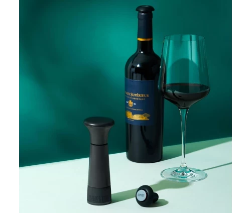 Innovine αντλία κενού αέρος για κρασί σε γκρι-μαύρο χρώμα με δύο επαναχρησιμοποιούμενα πώματα (κωδικός 12016), μπροστά από ποτήρι με κρασί.