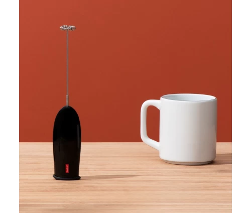 Bodum 3040-01 Schiuma χειροκίνητος αφροποιητής γάλακτος με μπαταρία σε μαύρο χρώμα, σε τραπέζι κουζίνας δίπλα σε κούπα καφέ.