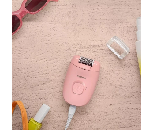 Η ροζ αποτριχωτική μηχανή Philips BRE227/00 σε μια flatlay σύνθεση με γυαλιά ηλίου, μανό και καλλυντικά.